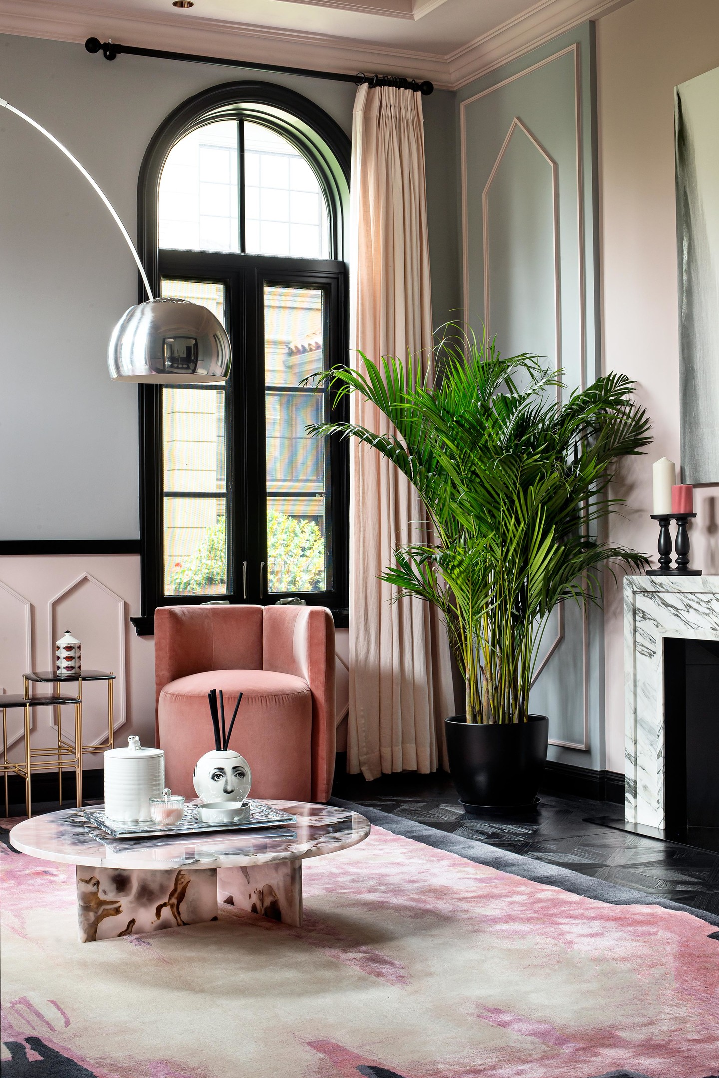 Phòng khách chính với gam màu hồng - đen chủ đạo, nội thất với những đường cong mềm mại từ khung cửa mái vòm, ghế sofa, ghế bành, bàn nước cho đến đèn sàn tinh tế.