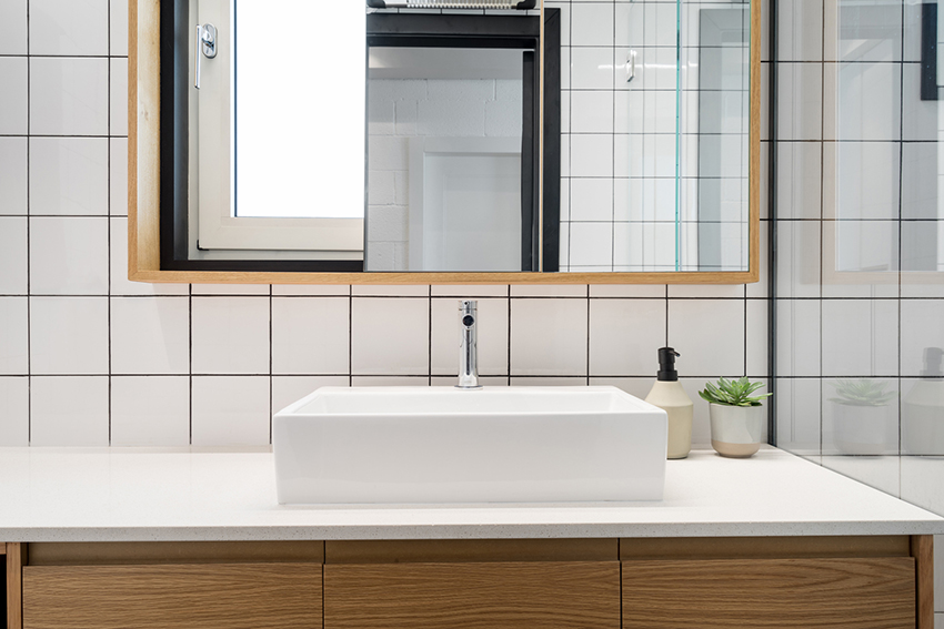 Phòng tắm sử dụng gạch ốp tường mosaic vuông màu trắng kích cỡ trung bình để lát tường, tủ vanity gọn đẹp cùng thiết kế tủ kết hợp cửa gương phía trên bồn rửa để lưu trữ và 'cơi nới' không gian nhỏ bằng thị giác.