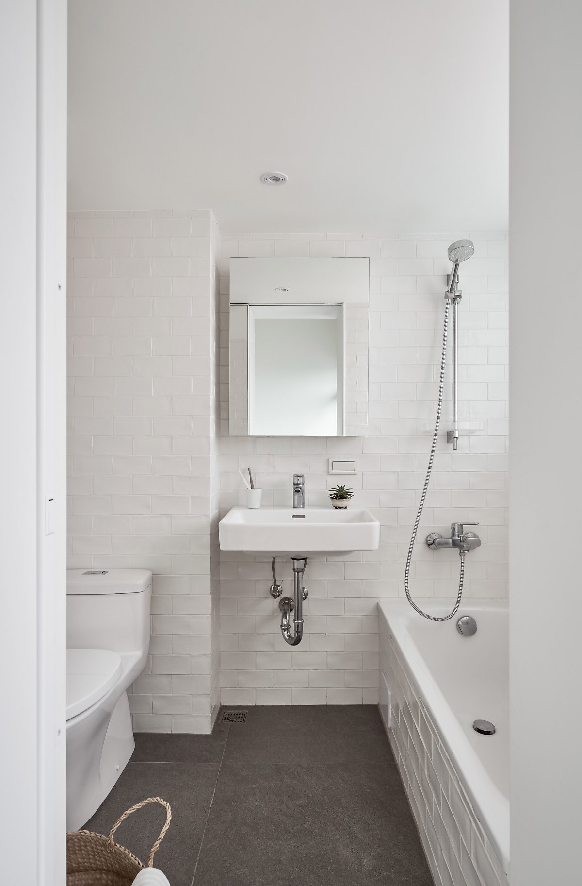 Phòng tắm tươi sáng nhờ sắc trắng của gạch ốp tường. Bồn rửa tay phân vùng toilet - bồn tắm một cách trực quan. Phía trên là tủ lưu trữ mặt gương giúp nhân đôi không gian và ánh sáng.