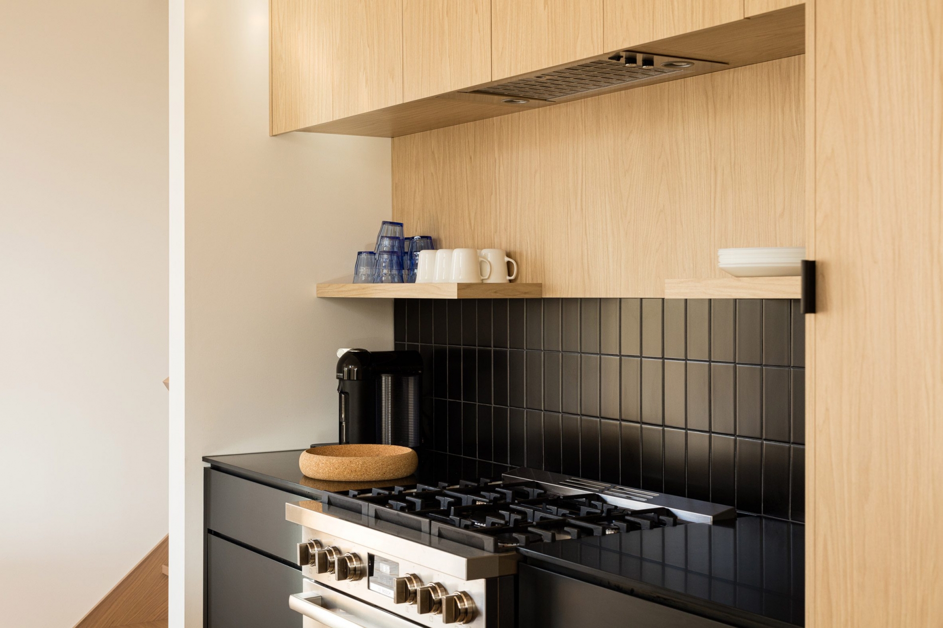 Phòng bếp là sự kết hợp hài hòa giữa nội thất gỗ tươi sáng và gam màu đen tuyền ở cả tủ bếp dưới, mặt bàn và gạch ốp backsplash cho cái nhìn sạch sẽ.