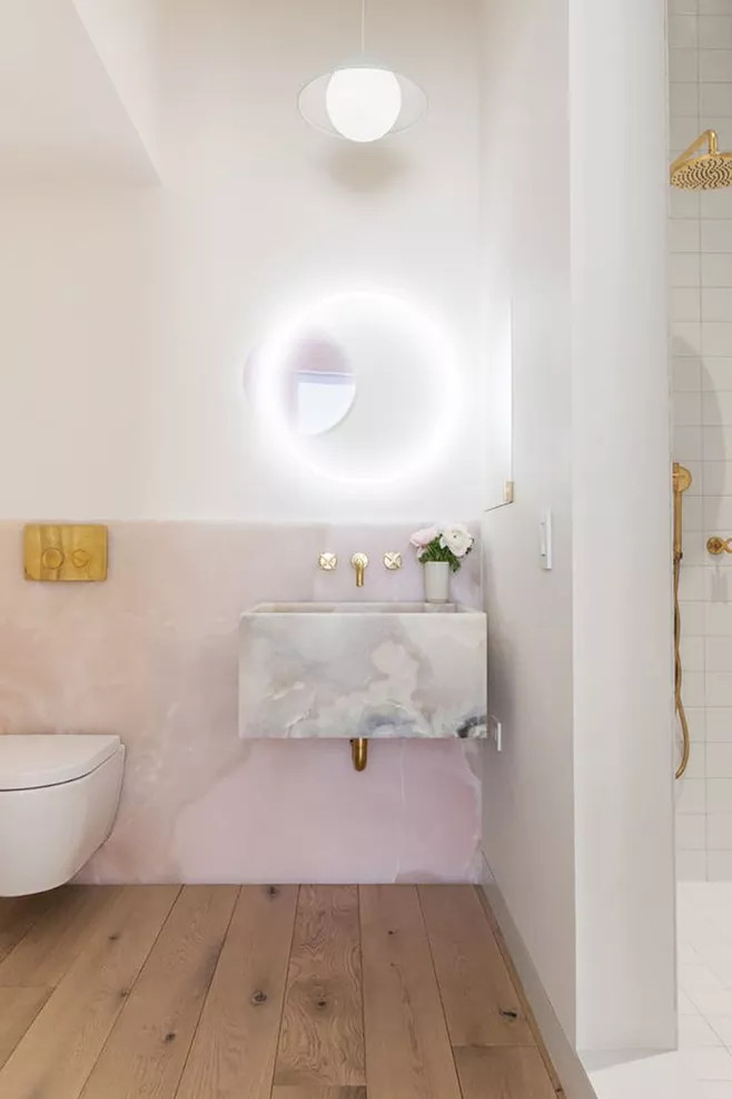Với chiếc gương tròn kết hợp đèn Led lung linh cùng vật liệu đá cẩm thạch hồng ốp tường tương phản nhẹ nhàng với gam màu trắng và bồn rửa cùng vật liệu làm tôn lên vẻ đẹp mộng mơ của phòng tắm.