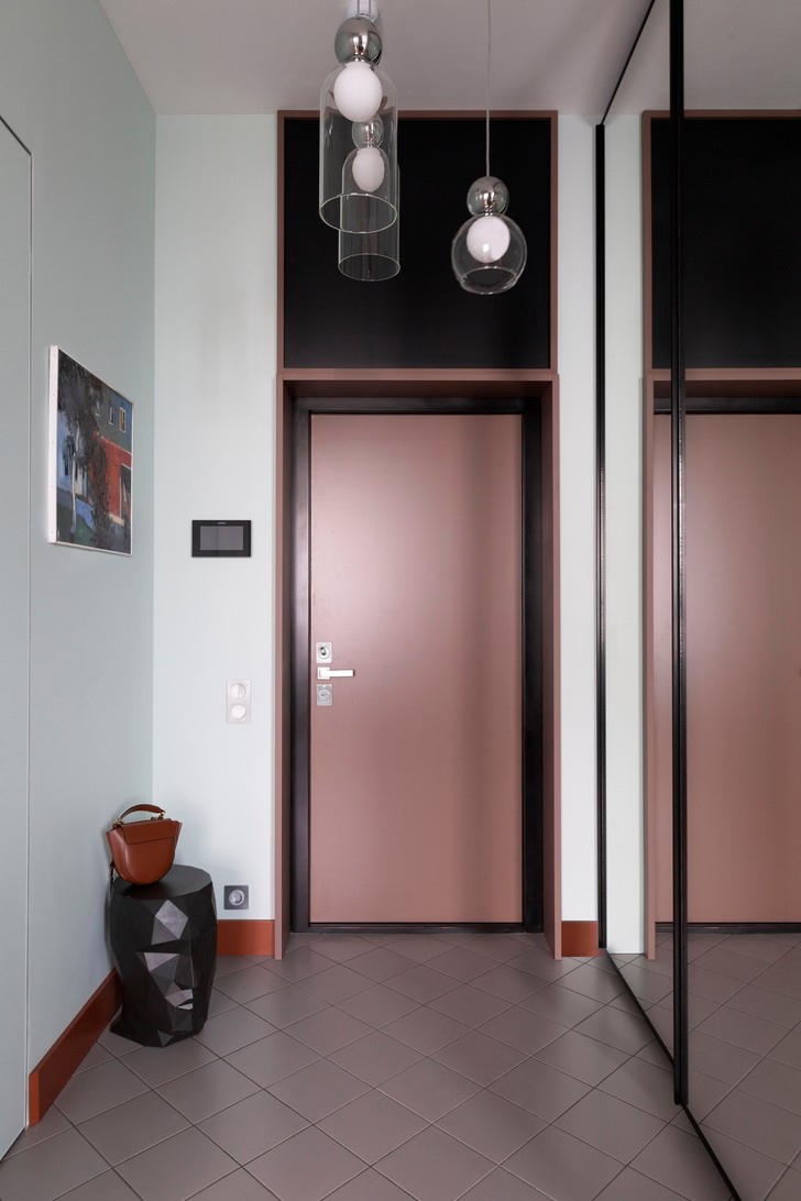 Lối vào căn hộ sử dụng 2 tone màu tím nhạt và đen ở cửa ra vào tạo sự tương phản mạnh mẽ. Một chiếc ghế đôn tạc kiểu mặt người độc đáo, trên tường là bức tranh cho thấy gu thẩm mỹ cá tính của chủ nhân.