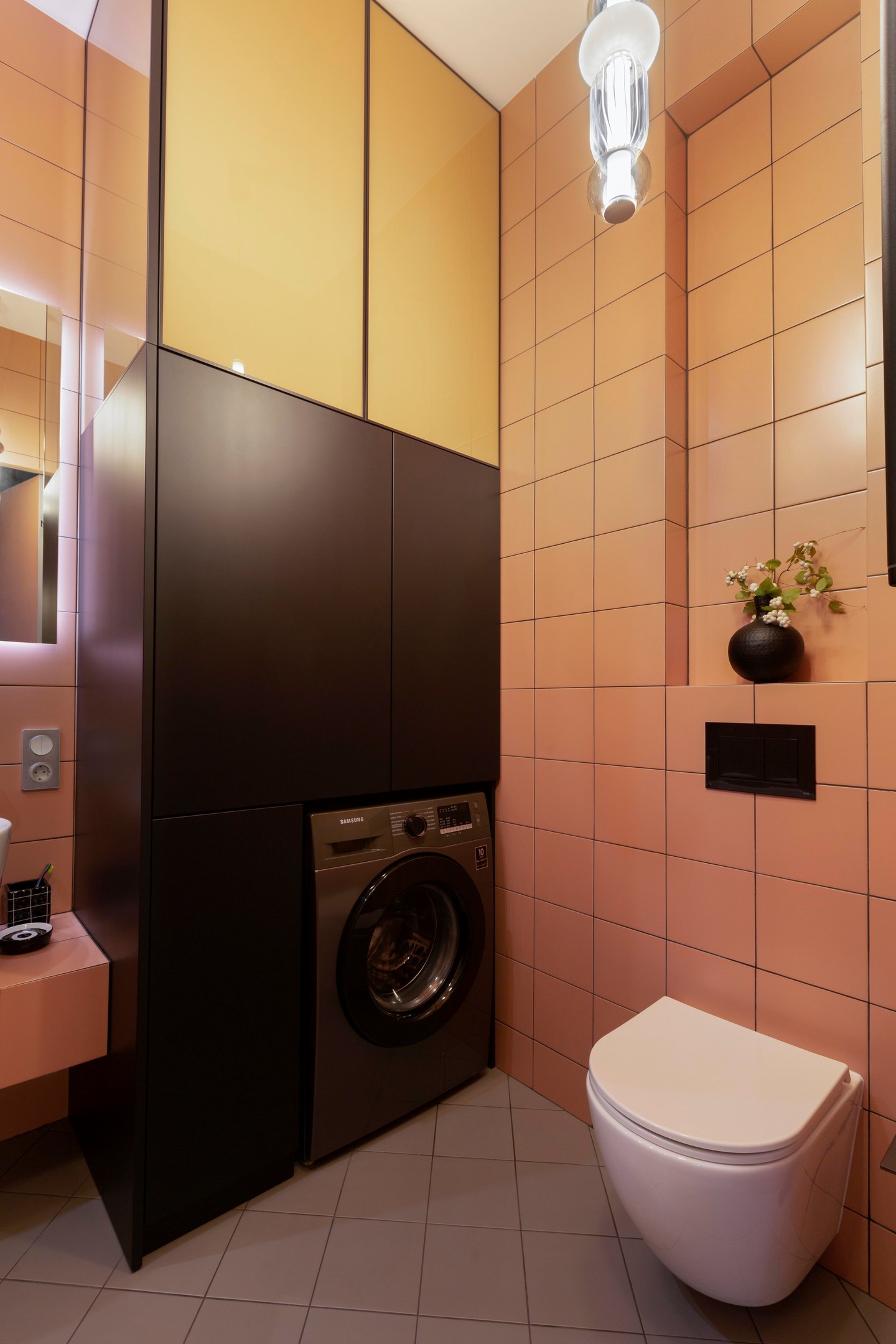 Có thể nói, mỗi khu vực chức năng trong căn hộ đều mang một màu sắc nổi bật để tạo sự khác biệt. Phòng tắm chọn gạch ốp tường màu gạch đất nung ấm áp, toilet gắn tường hiện đại, góc tường là tủ lưu trữ tích hợp không gian cho máy giặt.