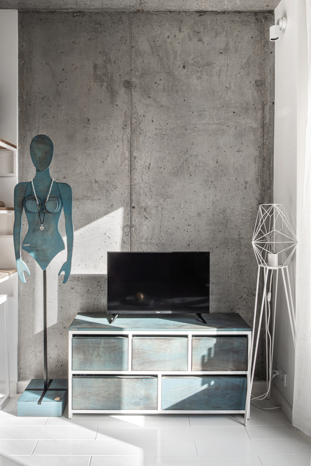 Tivi đối diện phòng khách được đặt trên chiếc tủ gỗ, bên cạnh là mô hình cô gái được làm bằng gỗ bạch dương với lớp sơn màu xanh cổ điển. 
