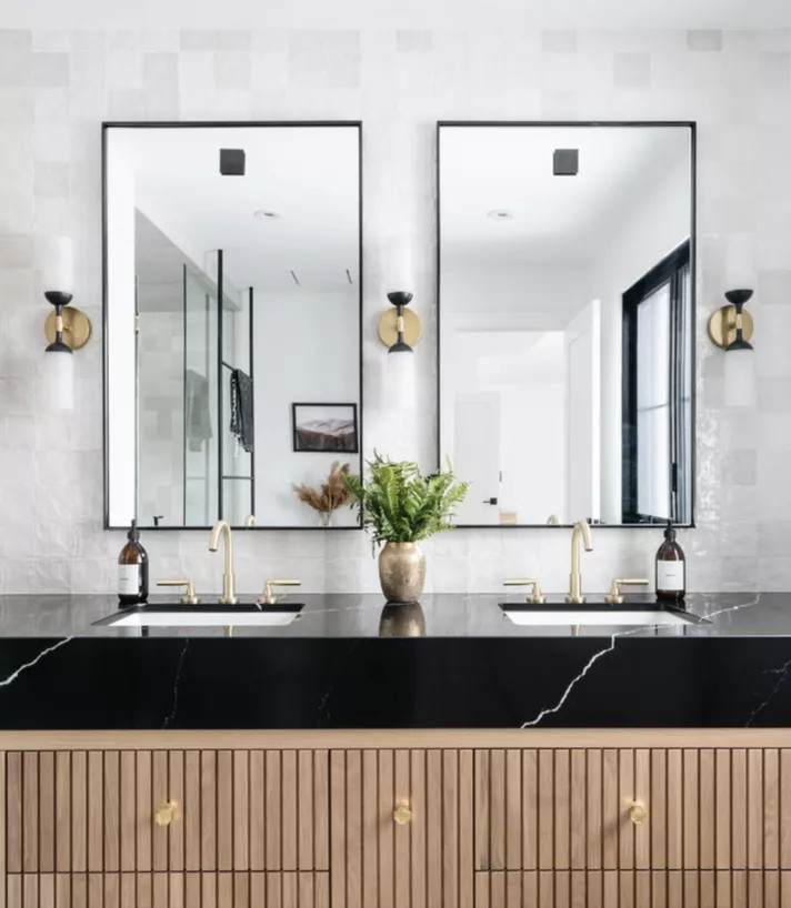 Bên cạnh màu sắc thì vật liệu cũng góp phần tạo nên sự đa dạng trong thiết kế phòng tắm. Ở đây, tường phòng tắm dùng gạch mosaic vuông màu trắng xám bóng đẹp, kết hợp tủ vanity gỗ và mặt bàn đá cẩm thạch đen siêu sang chảnh.