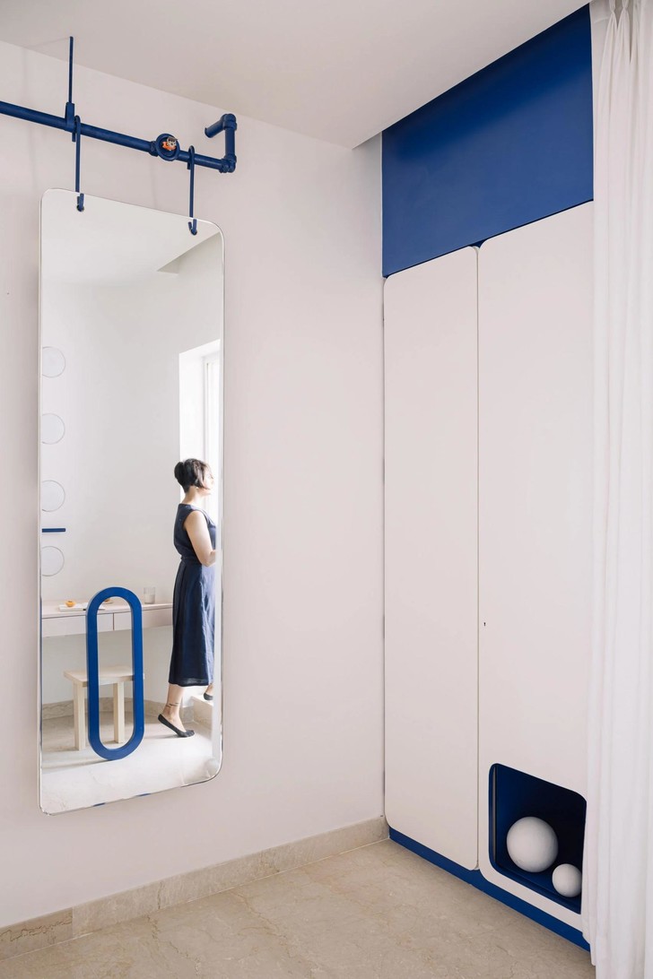 Hệ thống tủ lưu trữ mà trắng nổi bật với phông nền xanh coban phía sau, thể hiện sắc màu chủ đạo của căn hộ ngay tại khu vực hành lang lối vào.