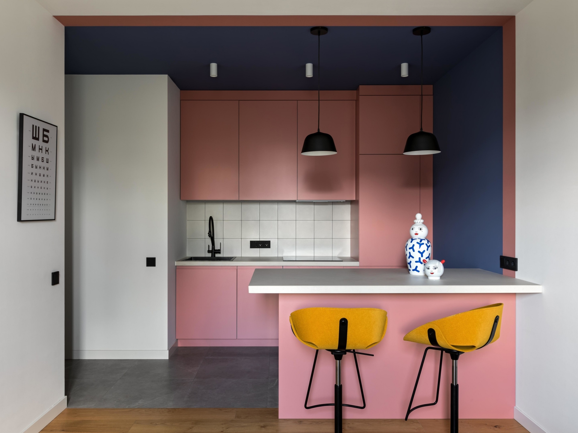 Phòng bếp và khu vực ăn uống thiết kế tối giản với hệ thống tủ lưu trữ và bàn ăn màu hồng phấn, xung quanh được bao bọc bởi bức tường xanh lam đậm. Ngoài ra còn bổ sung 2 chiếc ghế màu vàng mù tạt bắt mắt.
