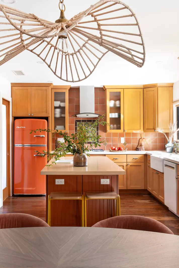 Phòng bếp đẹp như một bức tranh sinh động nhờ sự phối hợp các sắc thái khác nhau của màu cam: Chiếc tủ lạnh đậm màu bóng loáng, backsplash ốp gạch đất nung, hệ thống tủ bếp màu cam nhạt,... hòa quyện một cách hài hòa.