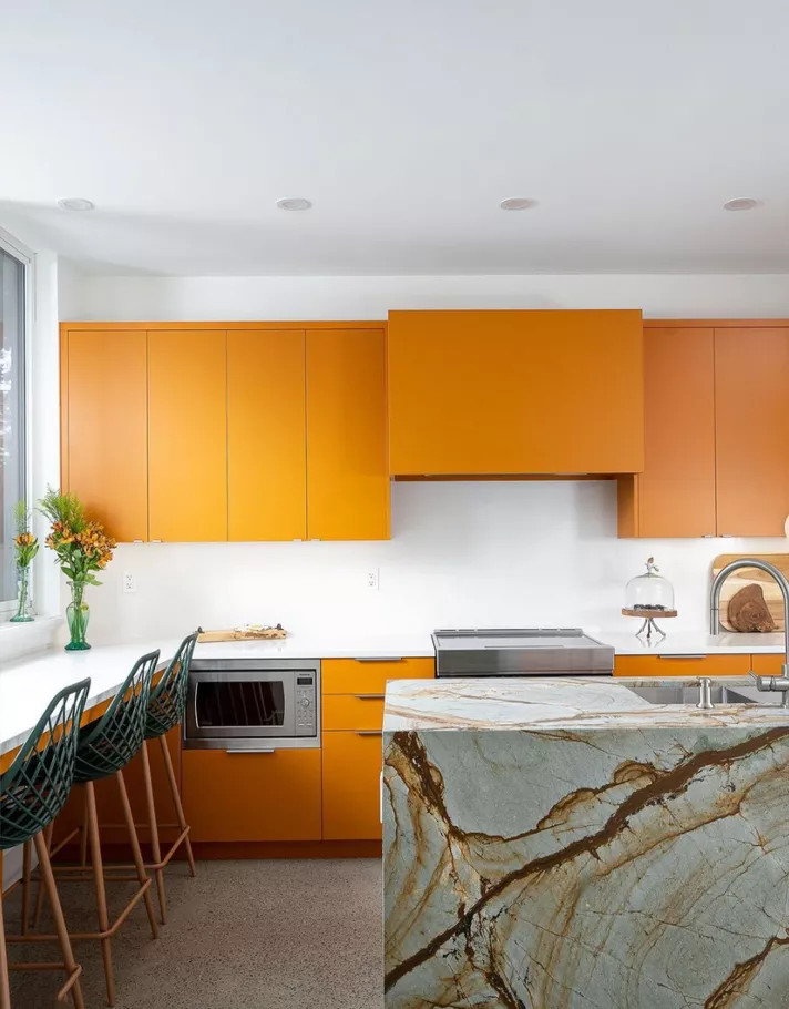 Không phải màu cam nào cũng chói lóa. NTK nội thất đã chọn hệ thống tủ bếp trên và dưới màu cam quýt tươi sáng, nổi bật trên phông nền trắng của trần, tường và đảo bếp bằng đá cẩm thạch xám xanh với đường vân nâu - cam đẹp mắt.