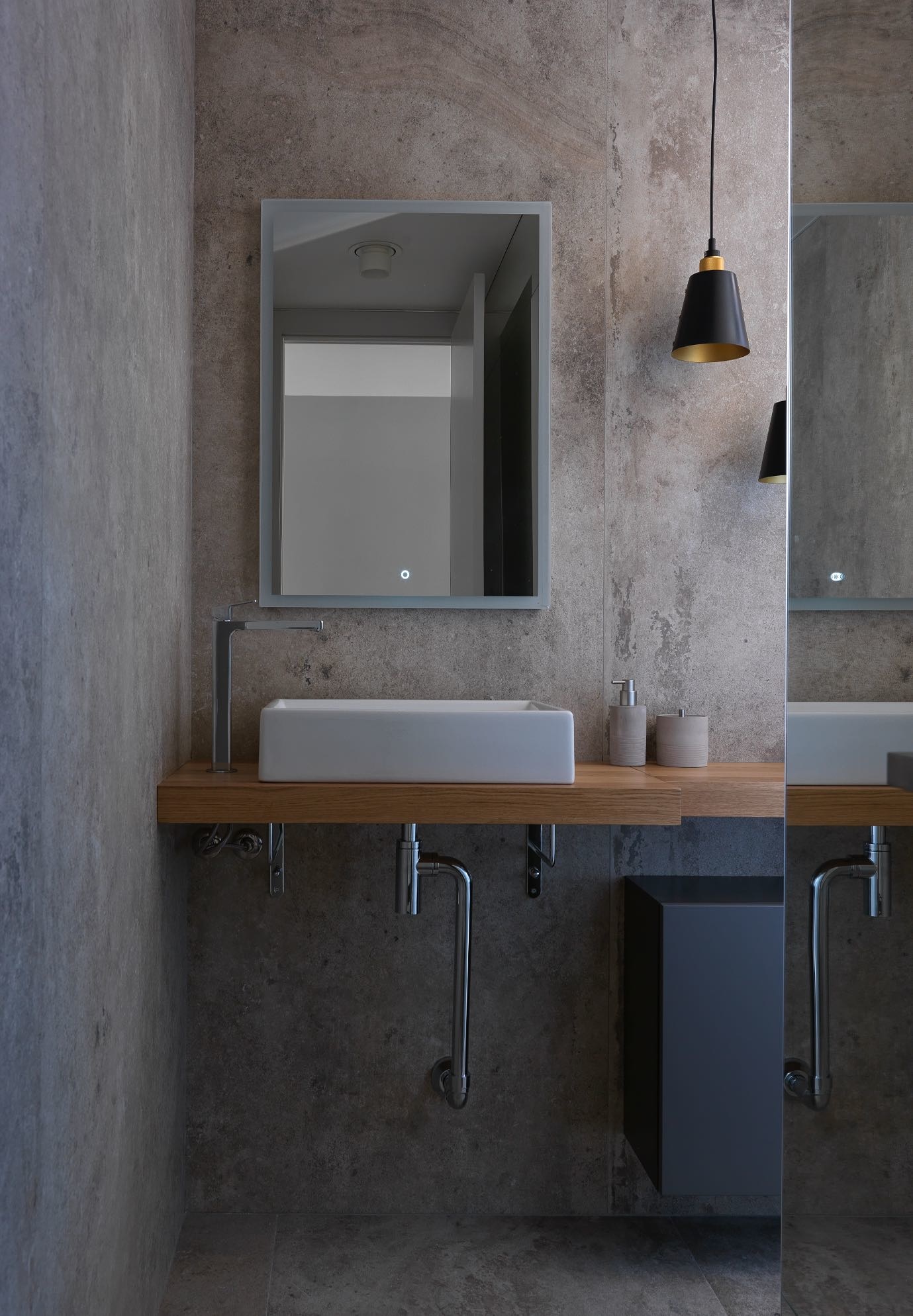 Nếu bạn yêu thích phong cách công nghiệp Industrial kết hợp Minimalism thì có thể tham khảo phòng tắm này để ứng dụng vào thực tế. Nó gọn gàng, đơn giản nhưng vẫn ấm áp nhờ kệ gỗ và đèn thả trần duyên dáng.