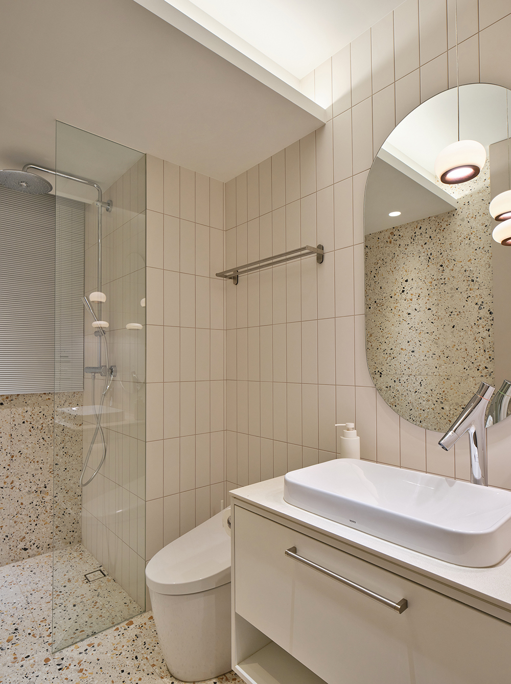 Phòng tắm và nhà vệ sinh cho khách sử dụng tone màu trắng - be chủ đạo, phân vùng bằng vách ngăn kính trong suốt cùng gạch ốp lát họa tiết terrazzo sinh động.