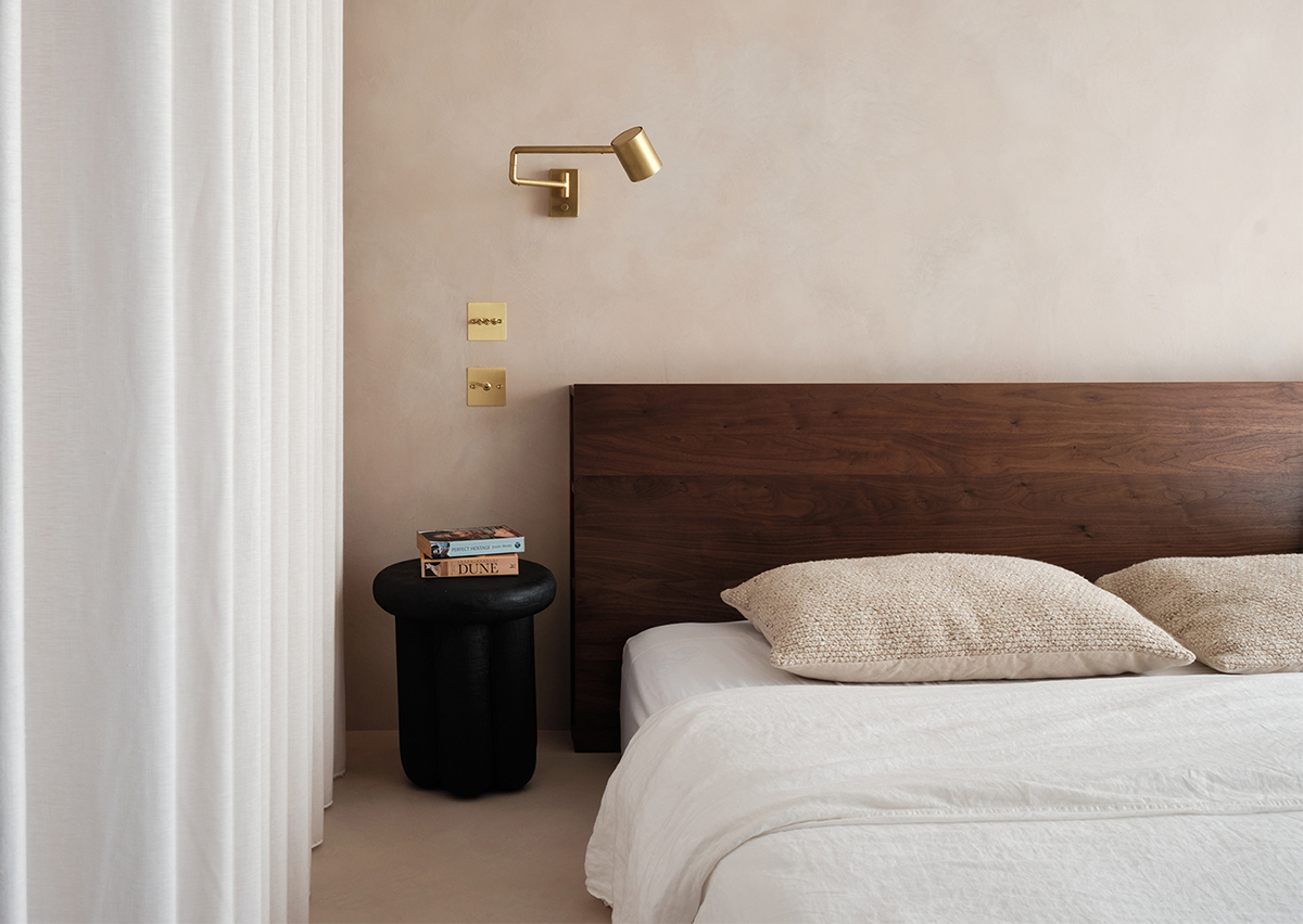 CănKhông gian phòng ngủ thiết kế theo phong cách tối giản với đầu giường gỗ vững chãi, táp đầu giường màu đen nhỏ gọn và đèn gắn tường mạ vàng đồng sang chảnh.
