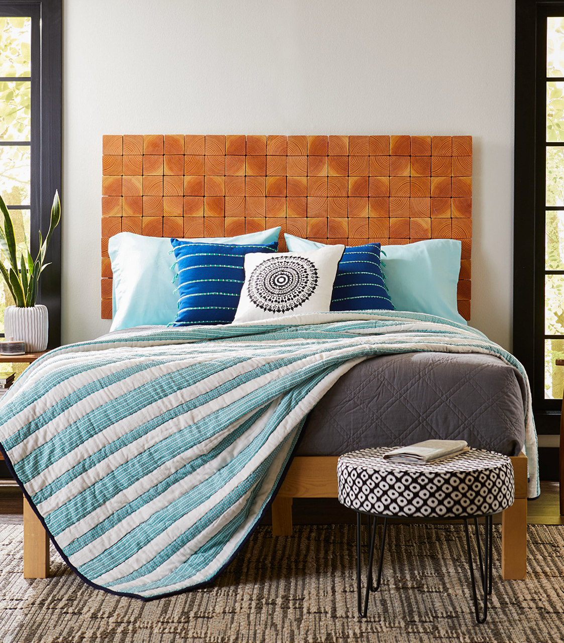 Đầu giường được ốp bằng những tấm gỗ MDF hình vuông nhỏ với đường vân trông rất tự nhiên, mang lại vẻ đẹp gần gũi và ấm áp, đồng thời tạo nên sự tương phản nhẹ nhàng với sắc xanh lam của chăn ga gối.