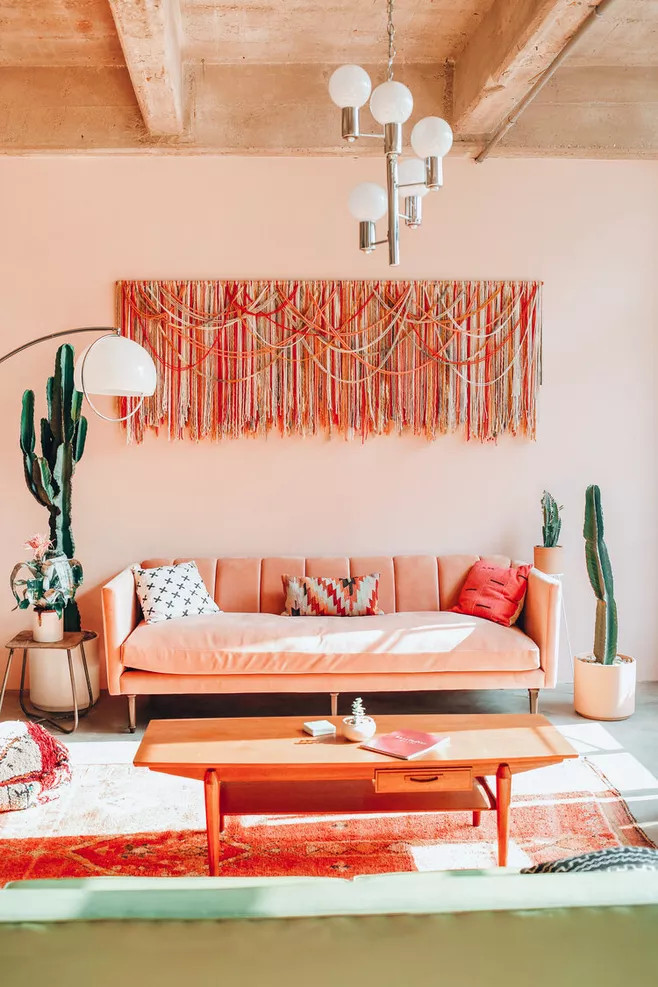 Có rất nhiều tình yêu màu sắc trong phòng khách mùa Xuân này! Ghế sofa màu cam san hô, tường sơn hồng phấn, thảm màu gạch đất nung, bàn gỗ ấm áp, thảm treo tường rực rỡ, thêm những chậu cây xương rồng xanh mạnh mẽ đầy sức hút.