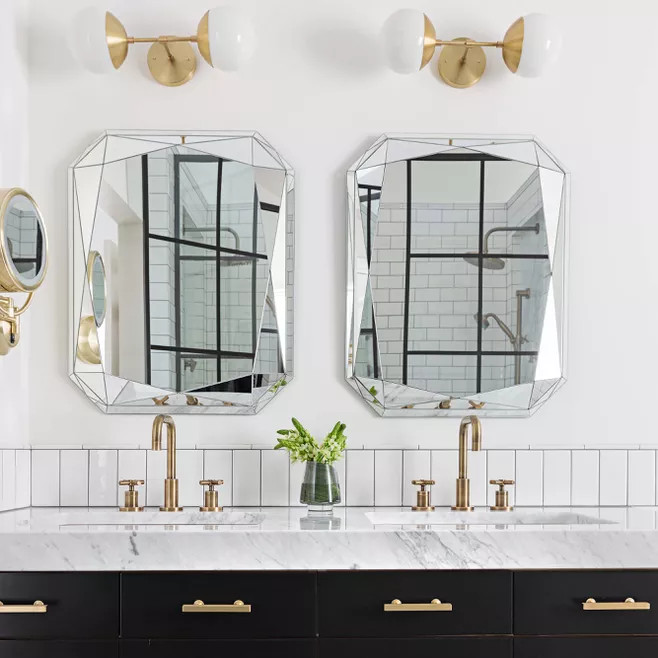 Cặp gương giống như những lăng kính phản chiếu ánh sáng và trang trí cho phòng tắm thêm độc đáo. Kết hợp với chúng là những chi tiết bằng kim loại mạ vàng đồng trên đèn gắn tường, gương soi hình tròn ở góc và hệ thống vòi rửa tay.
