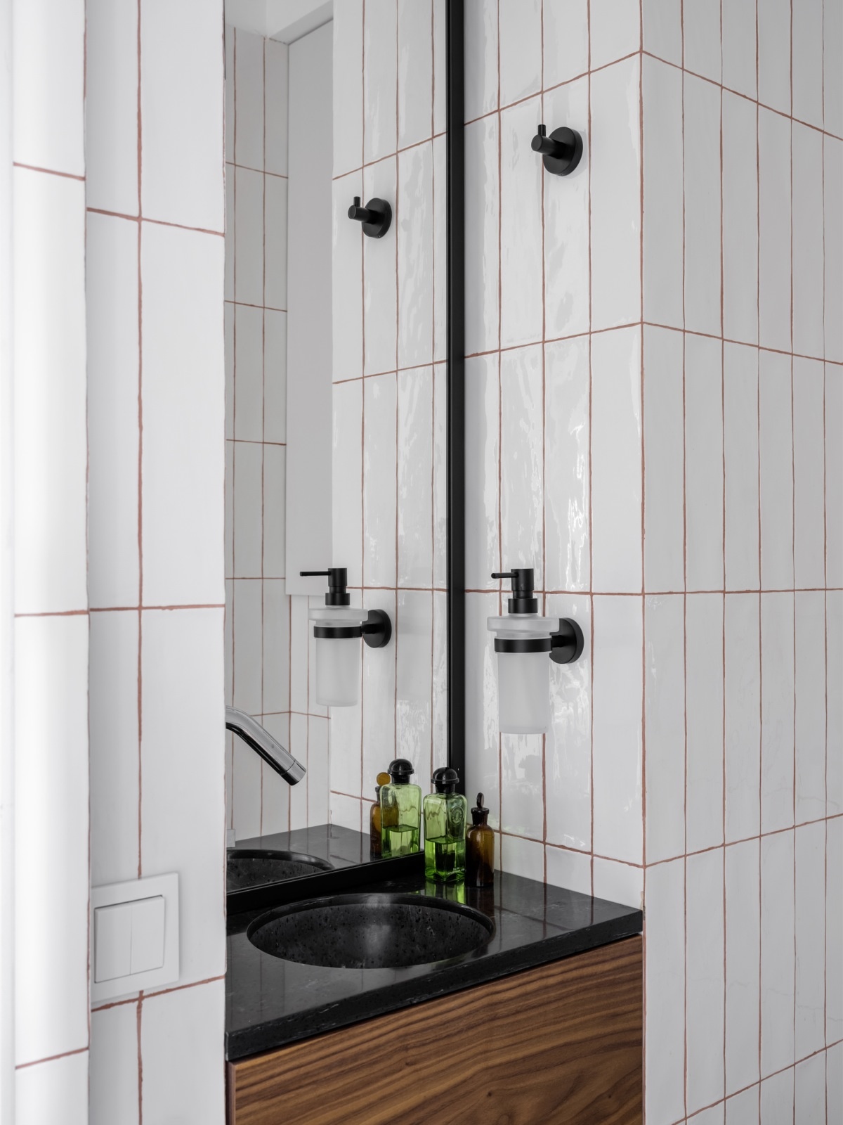 Phòng tắm nhỏ hẹp sử dụng gạch thẻ màu trắng ốp dọc tường để 'kéo cao' trần, với các đường kẽ gạch màu đỏ làm điểm nhấn. Nội thất màu đen cũng nhấn nhá chút sắc màu tương phản cho không gian.