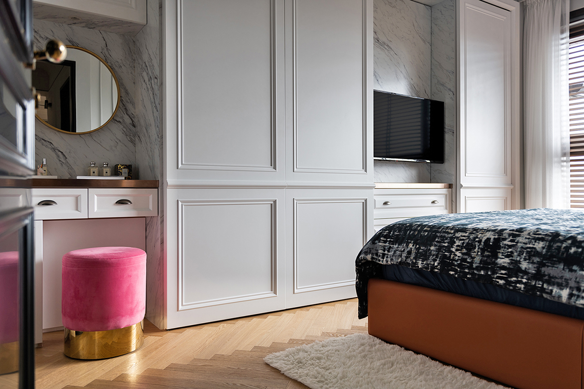 Đối diện giường ngủ là hệ thống tủ lưu trữ cao kịch trần, góc phải là bàn phấn trang điểm của người vợ với chiếc ghế đôn màu hồng điệu đà. Một chiếc tivi nhỏ cũng được bổ sung trên tường ốp đá cẩm thạch như phòng khách.