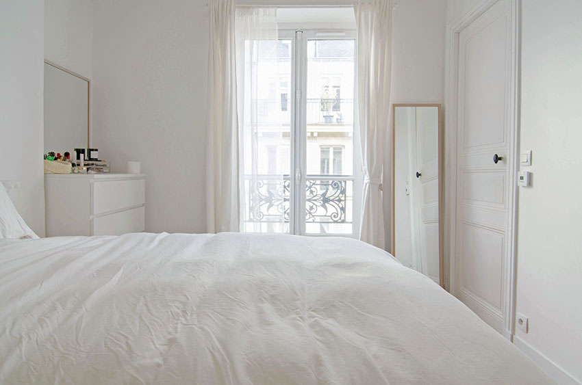 Không gian phòng ngủ chỉ sử dụng duy nhất một gam màu trắng với tấm gương hình chữ nhật khổ dọc đặt ở góc phòng. Bên cạnh giường ngủ là bàn phấn trang điểm gọn gàng. Tấm rèm che mỏng nhẹ giúp cản sáng khi trời nắng gắt.