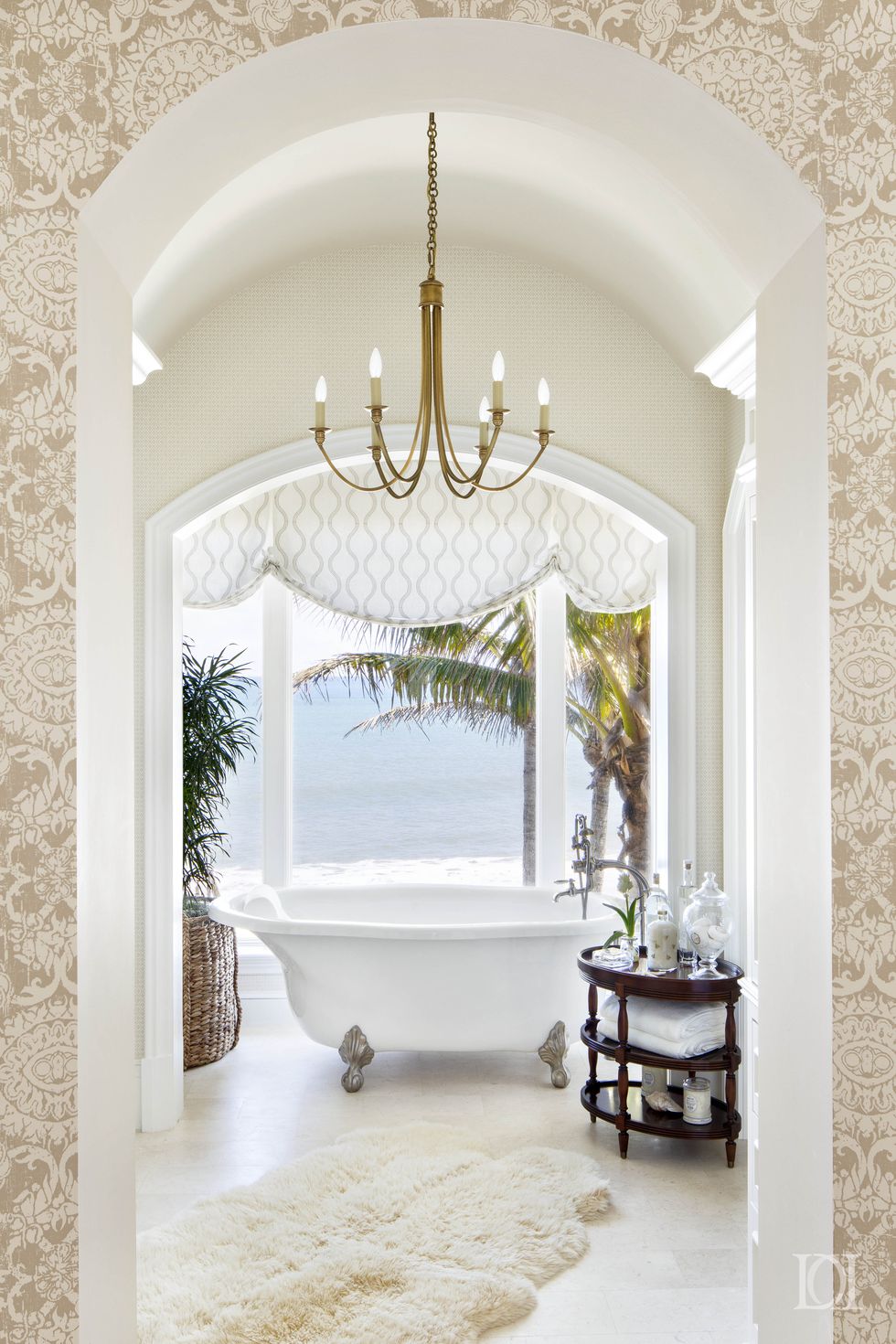 Phòng tắm thiết kế theo phong cách Địa Trung Hải với những ô cửa mái vòm duyên dáng, nội thất sang trọng với bồn tắm nằm, thảm chân, đèn chùm,... và đặc biệt là khung cảnh biển xanh và hàng dừa tươi đẹp bên ngoài.
