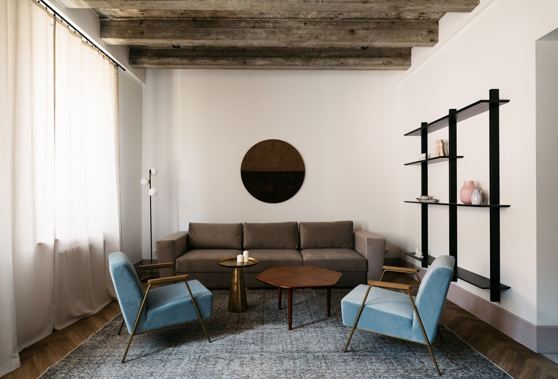 Phòng khách với bộ ghế sofa màu nâu cổ điển kết hợp ghế bành màu xanh ngọc lam tươi sáng, hiện đại, xếp đặt gọn gàng trên tấm thảm trải sàn cỡ lớn.