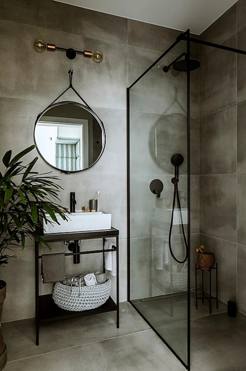 Phòng tắm sang trọng với gạch ốp tường màu xám nhạt, tấm gương tròn cổ điển, vách ngăn kính phân vùng buồng tắm đứng và bồn rửa cho cảm giác thông thoáng.