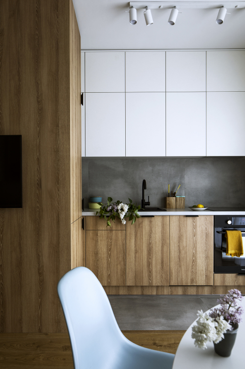 Phòng bếp thiết kế kiểu chữ I nhỏ gọn ở góc căn hộ, với sự tương phản giữa tủ bếp trên màu trắng và tủ dưới màu nâu của gỗ, chính giữa là backsplash màu xám đậm.