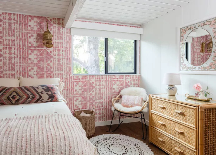 Trong phòng ngủ thiết kế theo phong cách Boho này, một bức tường với giấy dán họa tiết sắc hồng pha trắng tựa như một tấm thảm dệt mộng mơ trên tường, bên ngoài cửa sổ là khung cảnh cây cối tươi xanh.