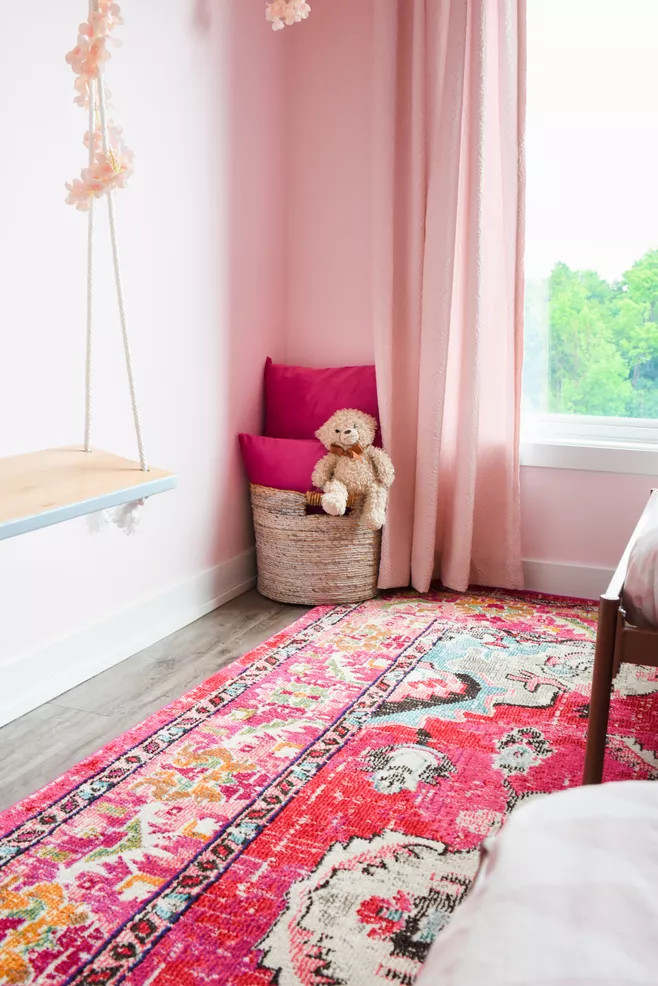 Nếu căn phòng của bé yêu đã sử dụng tấm thảm trải sàn họa tiết sặc sỡ với những tone màu hồng đậm như thế này thì cách tốt nhất để cân bằng lại chính là lựa chọn sơn tường và rèm che cửa sổ màu hồng phấn.