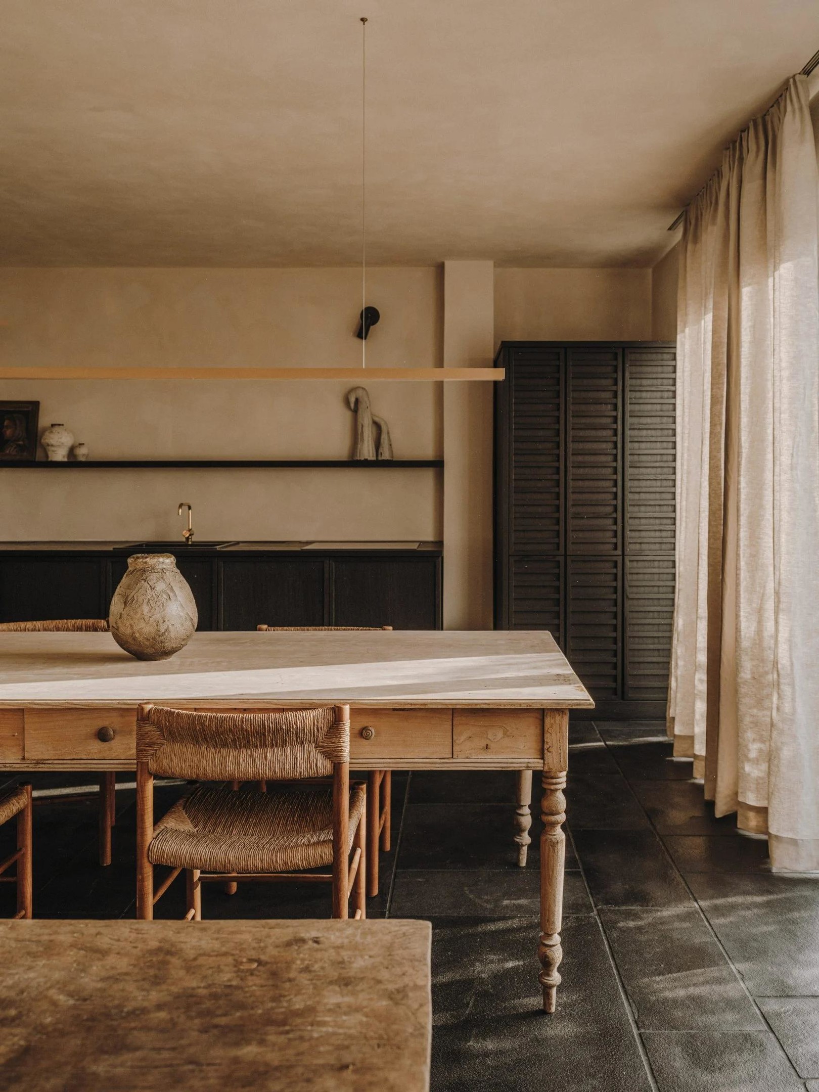 Phòng bếp thiết kế tối giản, kết hợp bàn ăn bằng gỗ kiểu dáng cổ điển, rèm che màu nâu cát mỏng nhẹ vừa đủ cản nắng gắt vừa tạo sự duyên dáng.