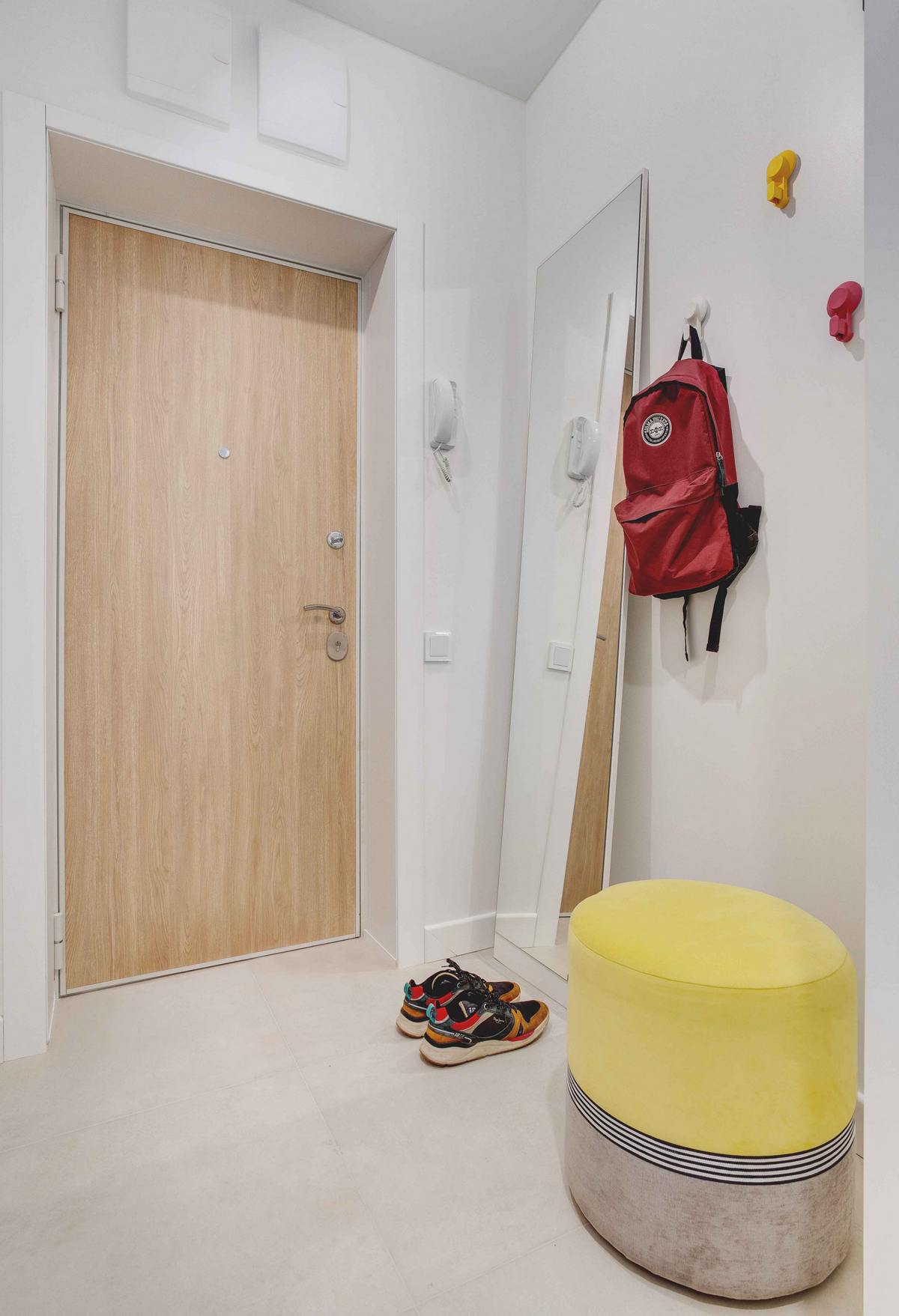 Lối vào căn hộ với cánh cửa gỗ ấm áp nổi bật trên phông nền trắng chủ đạo. Một tấm gương dài cùng những chiếc móc treo đồ nhỏ gọn, ghế đôn êm ái cho khu vực nhỏ thêm tiện nghi.