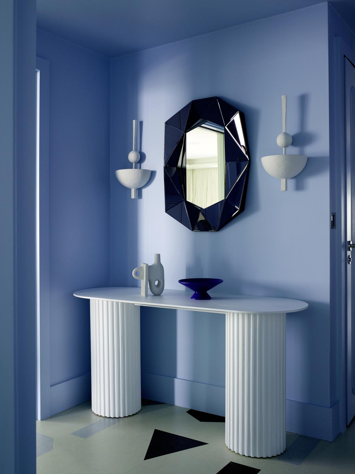 Giữa phông nền màu xanh lam êm dịu, tấm gương đa giác lồi với màu xanh coban 'đậm đặc' tạo nên một điểm nhấn hoàn hảo, đặt tại trung tâm 2 chiếc đèn gắn tường không kém phần đẹp mắt.