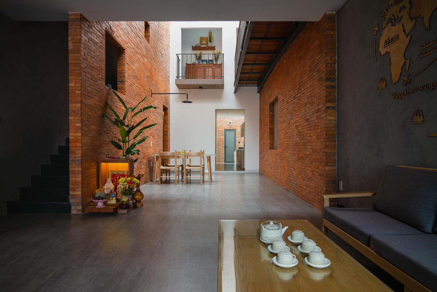 Không gian phòng khách với bộ bàn ghế tối giản, thiết kế liên thông với phòng ăn và phân tách bằng sự khác biệt của vật liệu ốp tường và bê tông - gạch thô.