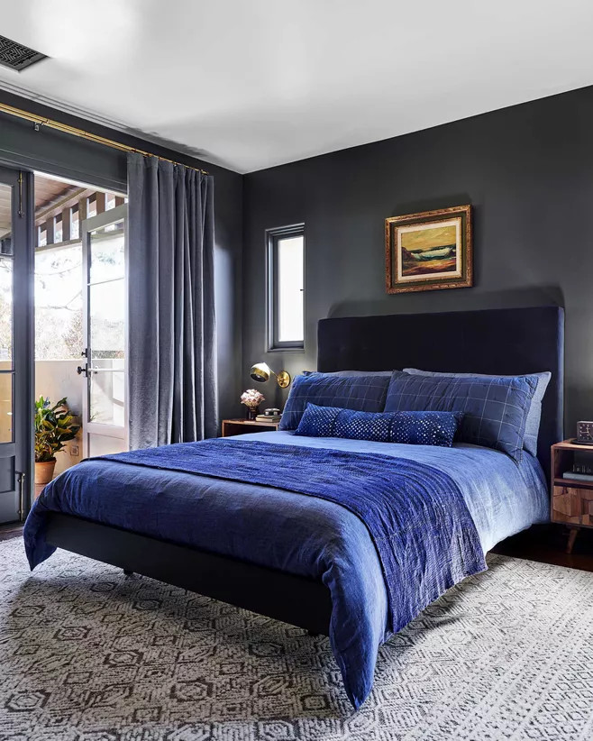 Mặc dù không sử dụng bất cứ tone màu nóng nào nhưng phòng ngủ vẫn toát lên vẻ đẹp ấm cúng. Màu xám than sơn tường kết hợp bộ ga giường sắc xanh lam đậm, rèm cửa xám nhạt và thảm trải sàn toàn bộ căn phòng cho cảm giác sang trọng tuyệt đối.