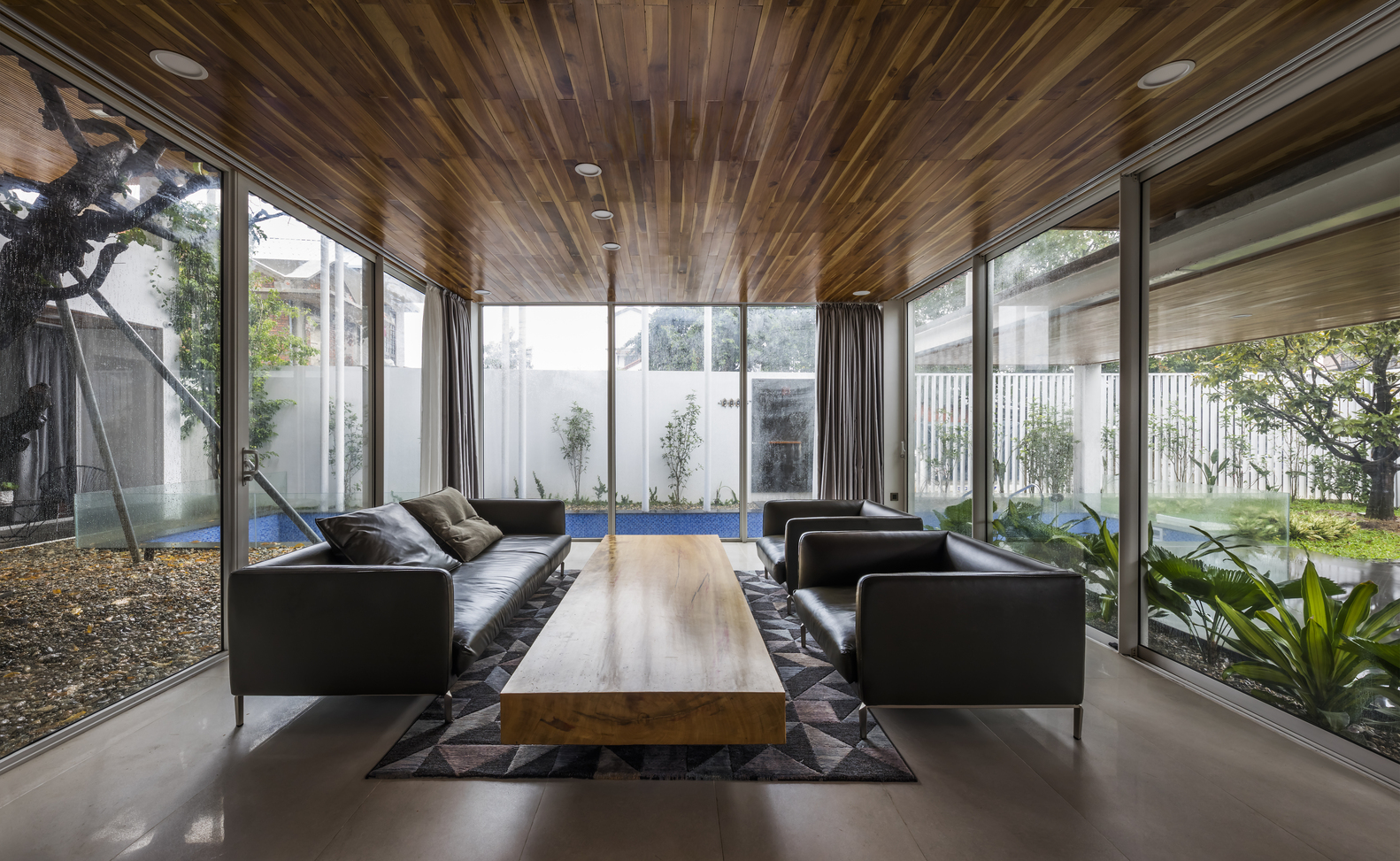 Phòng khách rộng rãi với nội thất tối giản nhưng sang trọng, bàn nước dài hình chữ nhật bằng gỗ vuông vức, ghế sofa bọc da êm ái đắt đỏ.