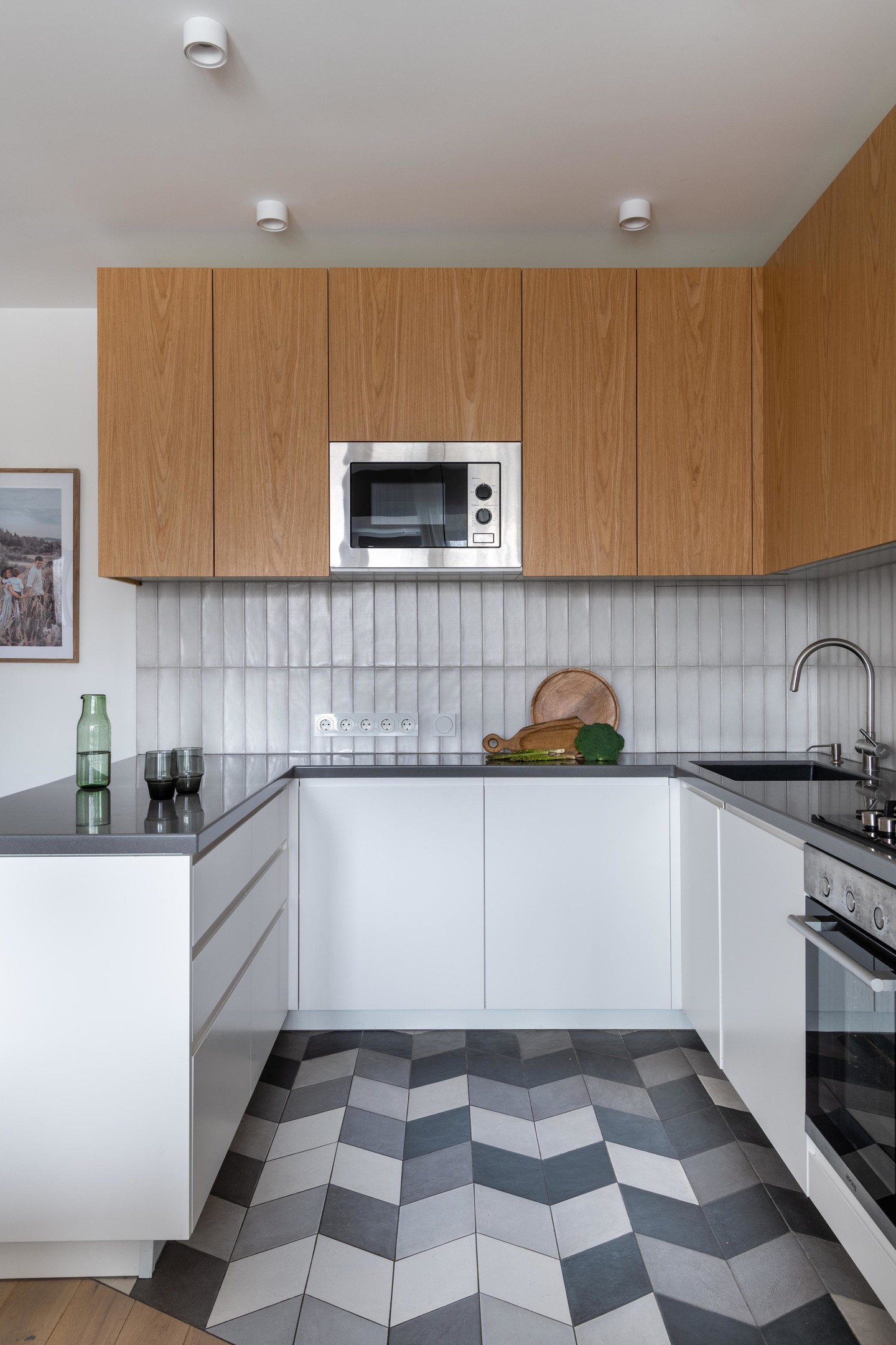 Phòng bếp nhỏ nhưng ấn tượng bởi cách NTK lựa chọn gạch ốp tường và lát sàn. Nếu gạch sàn nhà được sắp xếp cho cảm giác 3D sống động thì backsplash lại nhẹ nhàng, tối giản với gạch thẻ ốp dọc, ăn gian chiều cao cho phòng bếp.