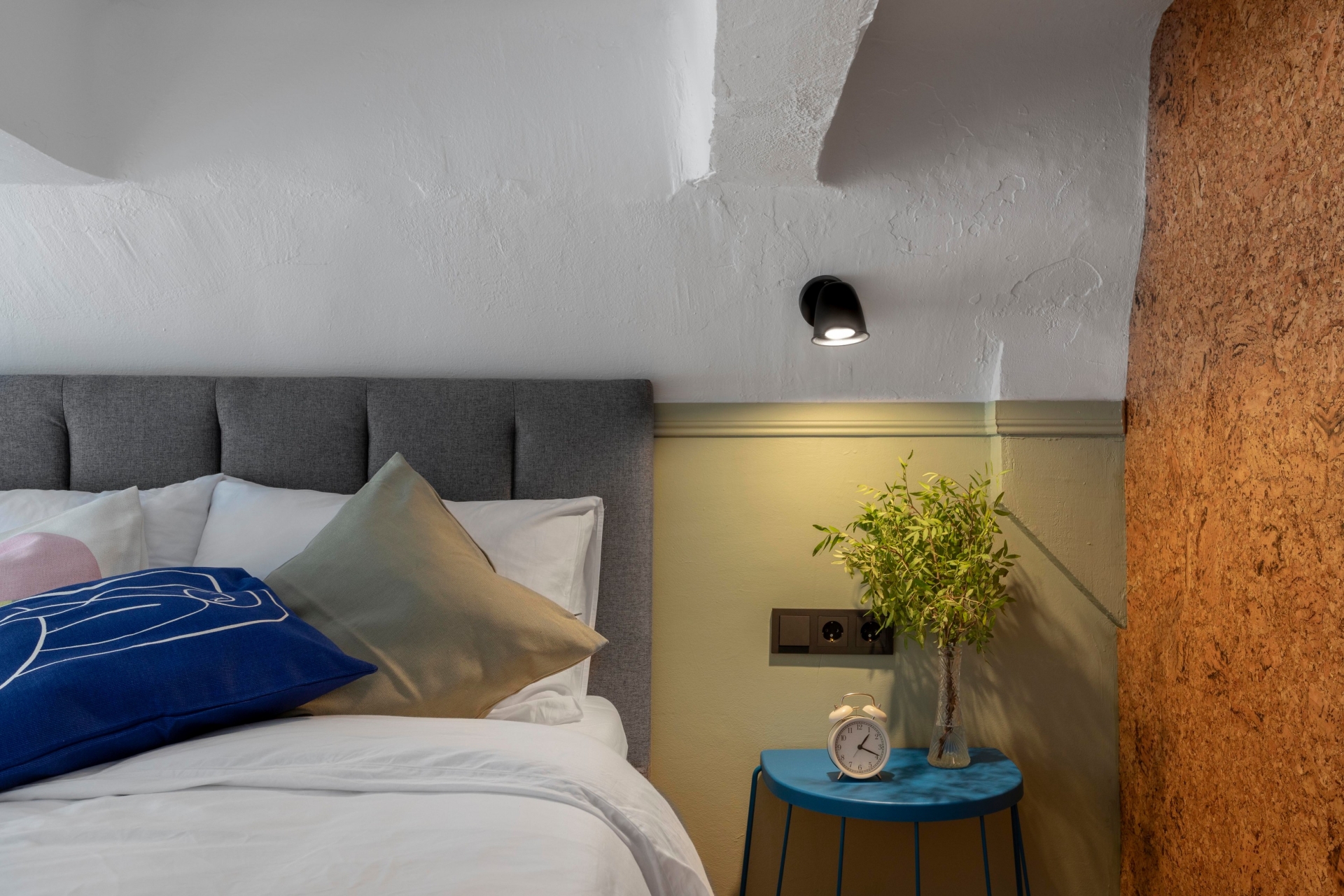 Không gian phòng ngủ được bố trí tách biệt trên gác lửng, tuy nhỏ nhưng tiện nghi với đầy đủ đèn gắn tường, táp đầu giường, lọ cây cảnh sống động. Thêm vào đó một bề mặt tường ốp gỗ bần để chủ nhân có thể tùy ý ghim hình ảnh, ghi chú hoặc trang trí theo sở thích.