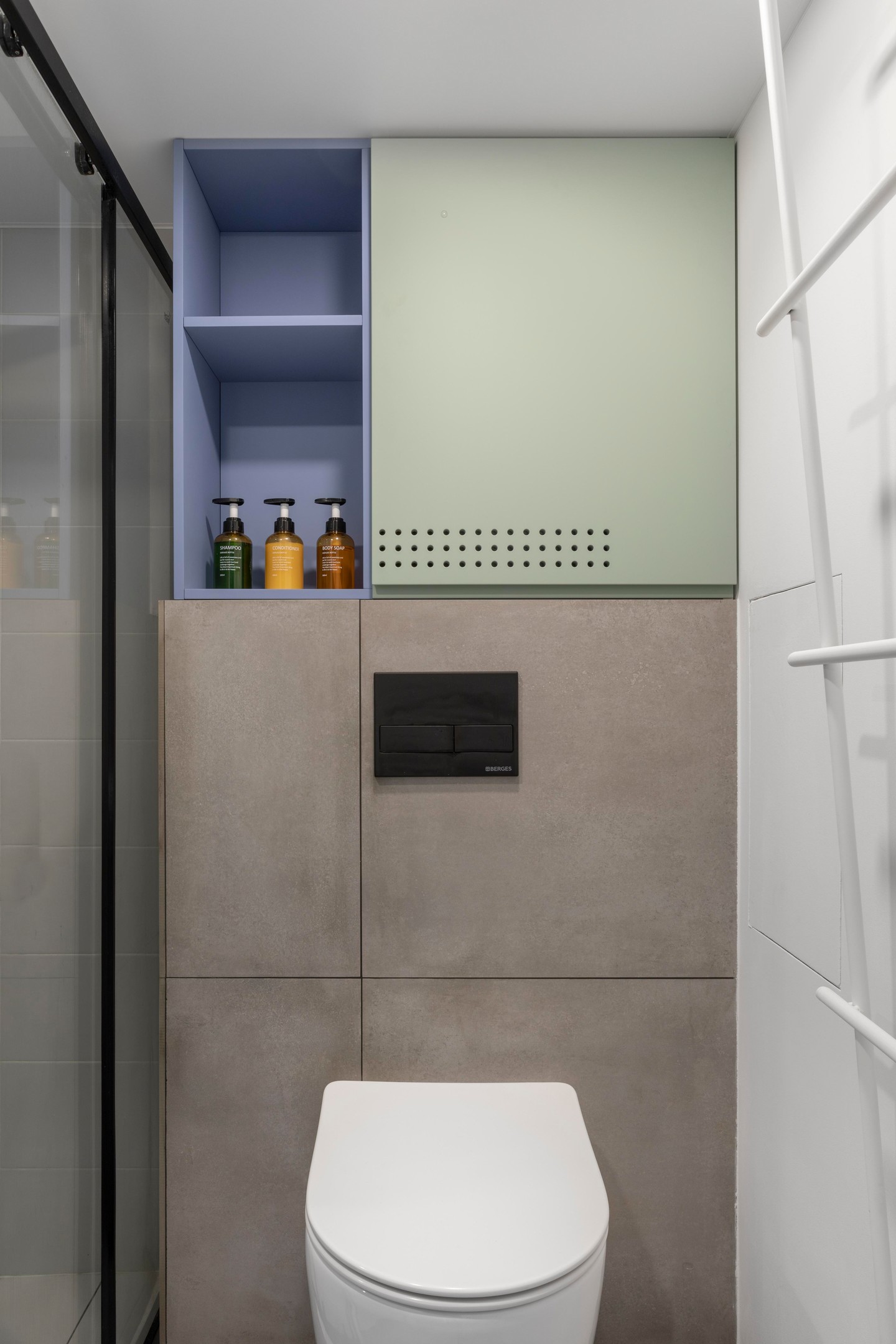 Toilet và phòng tắm được phân vùng bằng cửa trượt kính trong suốt. NTK lựa chọn kiểu bồn toilet gắn tường để tiết kiệm diện tích, đồng thời phía trên tường cũng bổ sung hệ thống tủ lưu trữ sơn sắc màu nhẹ nhàng và đẹp mắt.