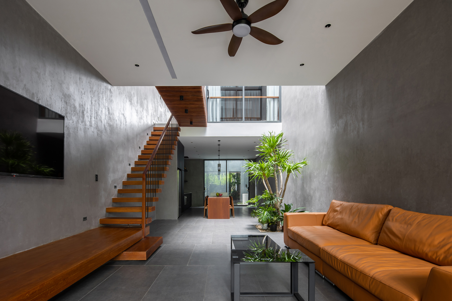 Phòng khách thiết kế tối giản với bộ ghế sofa màu nâu da bò êm ái, đối diện là tivi treo tường, tone màu xám kết hợp nâu gỗ cho cái nhìn ấm áp.