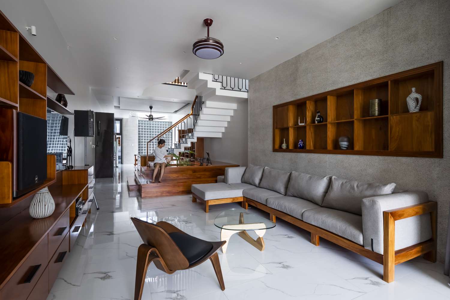 Phòng khách và bếp thiết kế mở với nội thất gỗ sang trọng. Ghế sofa dài bố trí sát tường, kệ mở lưu trữ gọn gàng, bàn nước mặt kính trong suốt giúp 'cơi nới' không gian.