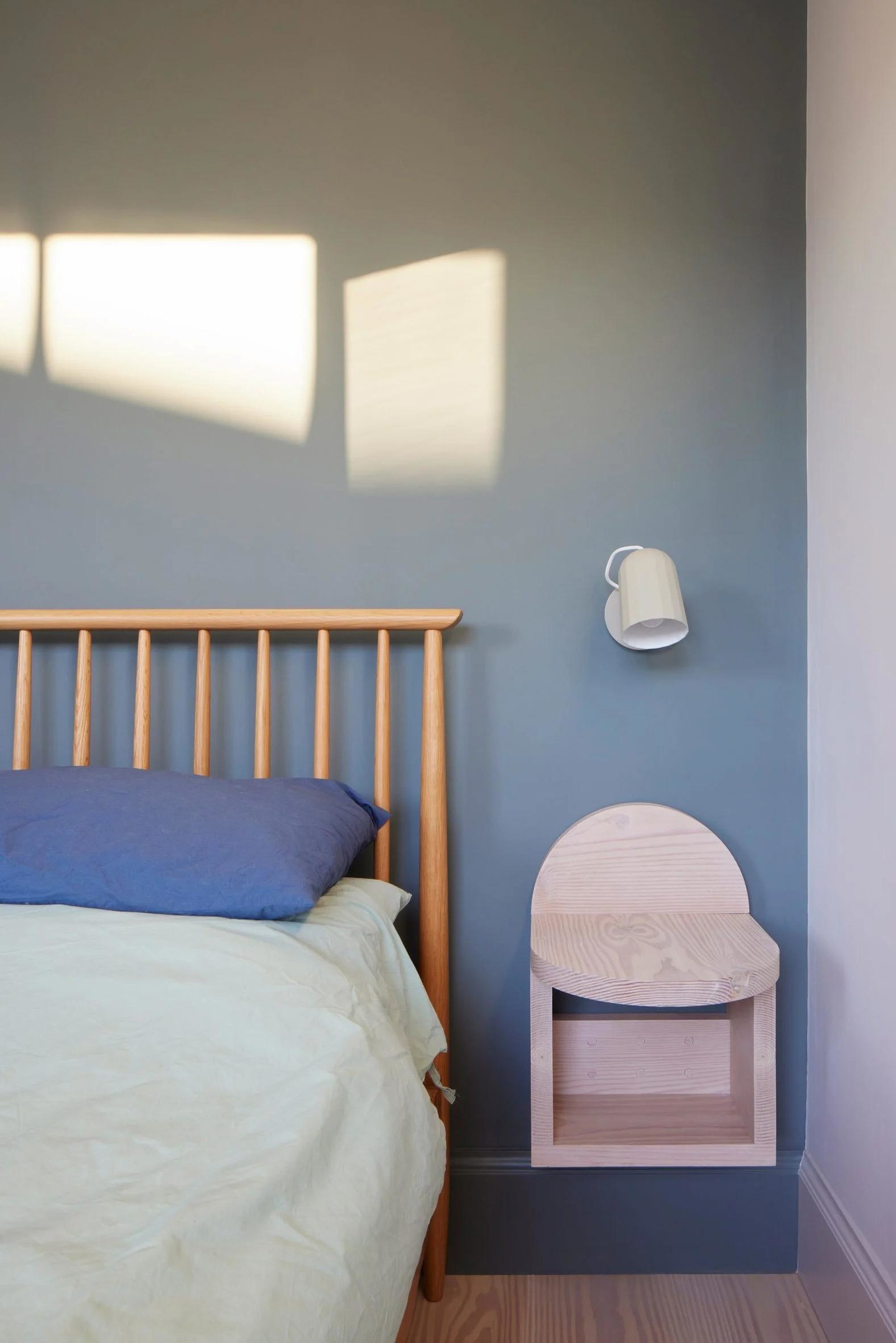 Nội thất phòng ngủ được thiết kế tối giản với giải pháp gắn tường giúp giải phóng mặt sàn như đèn ngủ, táp đầu giường đối xứng 2 bên. Loại gỗ làm táp đầu giường cũng là gỗ thông như ở góc làm việc.