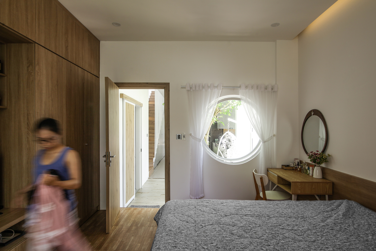 Cửa sổ phòng ngủ hình tròn cho phép chủ nhân có thể ngắm nhìn không gian bên ngoài xích đu và phòng bếp, đồng thời tạo sự liền mạch giữa các khu vực chức năng riêng biệt.
