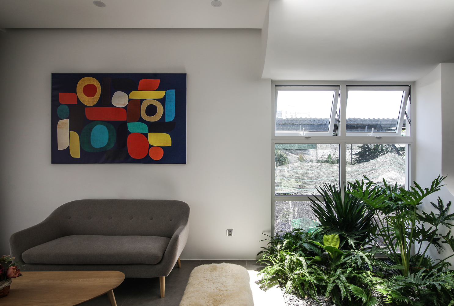 Không gian phòng khách nhẹ nhàng cùng ghế sofa và bàn nước thiết kế với đường cong mềm mại, trên tường là bức tranh trừu tượng làm điểm nhấn về màu sắc.
