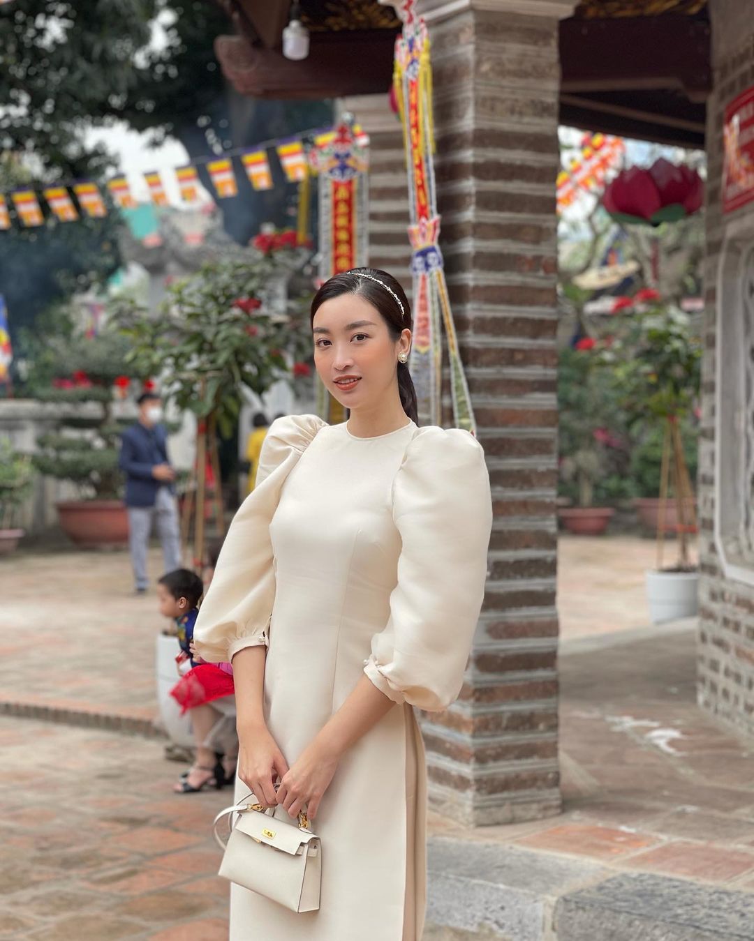 Hoa hậu Đỗ Mỹ Linh cũng đi lễ chùa cầu bình an trong năm mới. Cô diện chiếc áo dài cách tân màu sữa kết hợp với túi xách cùng màu & băng đô cài tóc đính đá rất duyên dáng và nữ tính
